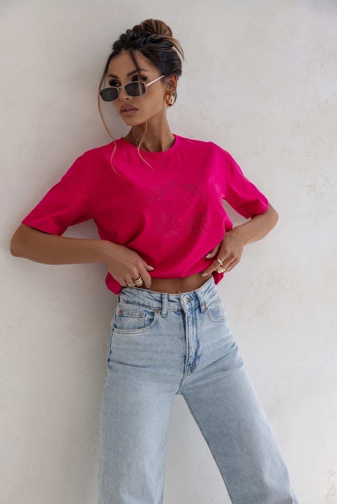 Woman wearing a bright pink t-shirt and light blue jeans against a white wall.