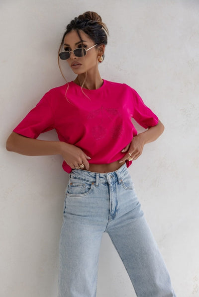 Woman wearing a bright pink t-shirt and light blue jeans against a white wall.