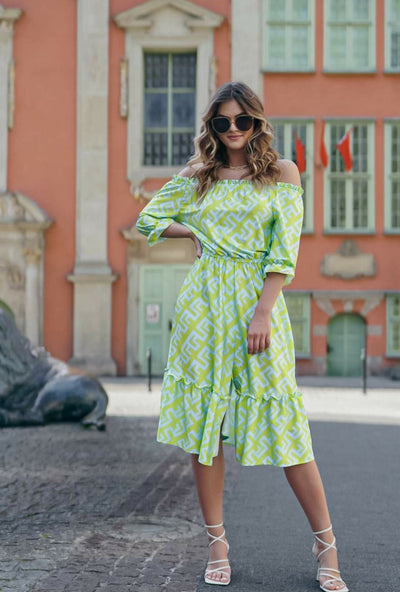 Woman in a green and white patterned dress standing on a street with a building in the background