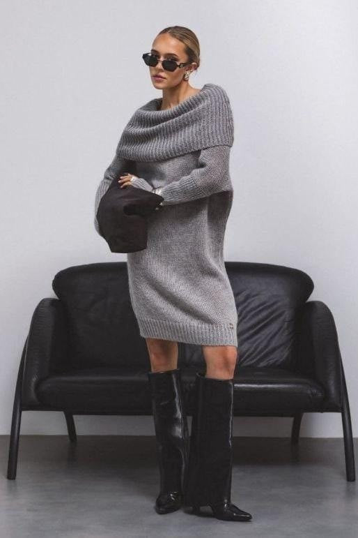 Woman wearing a gray sweater dress and black knee-high boots in a minimalistic setting.