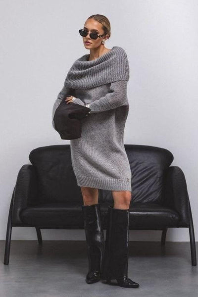 Woman wearing a gray sweater dress and black knee-high boots in a minimalistic setting.