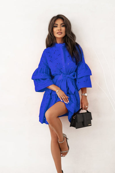 Woman wearing a blue dress holding a black handbag against a white background