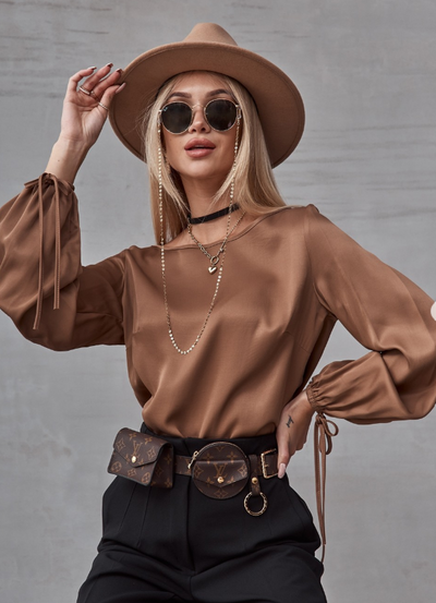 Woman wearing a brown outfit with a hat and sunglasses against a gray background