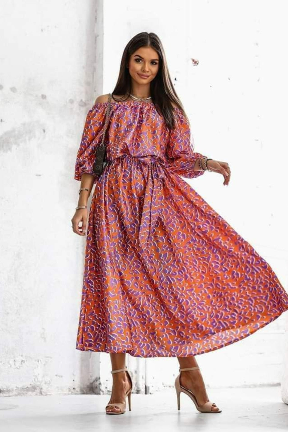 Woman wearing a patterned dress standing against a white wall.
