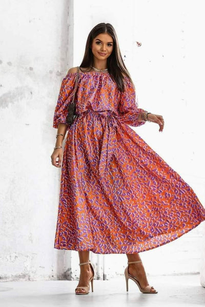 Woman wearing a patterned dress standing against a white wall.