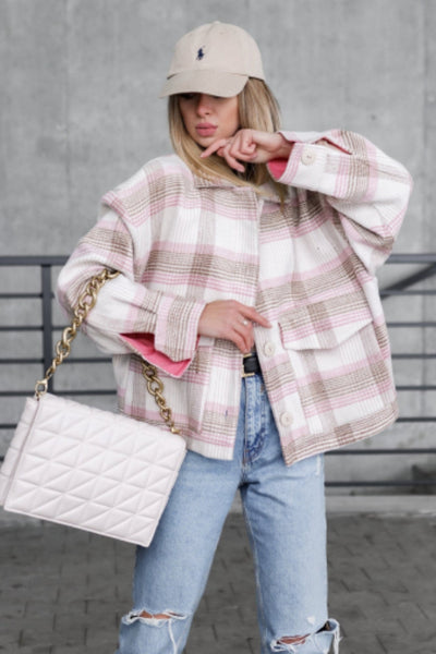 Person wearing a plaid jacket, light blue jeans, and a beige cap, holding a white quilted handbag.